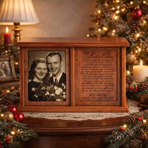 May include: A wooden memorial box with a framed photo of a couple on the left and a poem on the right. The box is brown and sits on a table decorated with Christmas ornaments and lights.