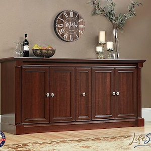 May include: A dark wood cabinet with six doors and silver door knobs. The cabinet is sitting on a wooden floor with a rug in front of it. A clock with the text "Miller" is hanging on the wall above the cabinet.