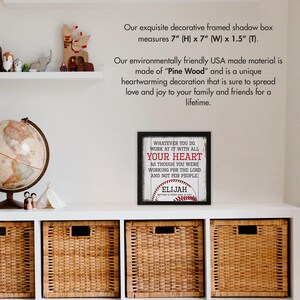 May include: A framed shadow box with a baseball-themed quote: "Whatever you do, work at it with all your heart as though you were working for the Lord and not for people." The quote is printed on a white wood background with a red baseball and the name "Elijah" printed below. The frame is black and measures 7 inches by 7 inches.