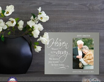 May include: A gray picture frame with a white inscription that reads "If Heaven Wasn't So Far Away We Know You Would Be Here Today." The frame has a photo of an older couple in the center. The inscription is in a cursive font. The frame is on a wooden surface.