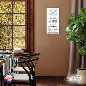 May include: A white wood sign with black text that reads "Kitchen Rules: Family & Friends Always Welcome, Give Thanks, Kiss The Cook, Smell The Love, Mind Your Manners, Offer To Help, Eat Together, Clean Up After Yourself".