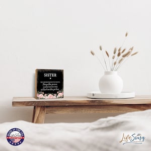 May include: A black wooden sign with white text that reads "Sister, You are braver than you believe, stronger than you seem, smarter than you think, and loved more than you know." The sign is decorated with pink flowers.