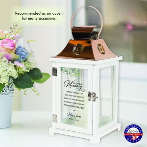 May include: White lantern with a copper top and glass panels. The glass panels feature a floral design and a memorial message that reads "In Loving Memory." The lantern has a quote about those we love and a personalized name and dates.