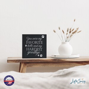 May include: Black wooden sign with white text that reads "You were my FAVORITE hello and my HARDEST goodbye" with paw prints around the text.