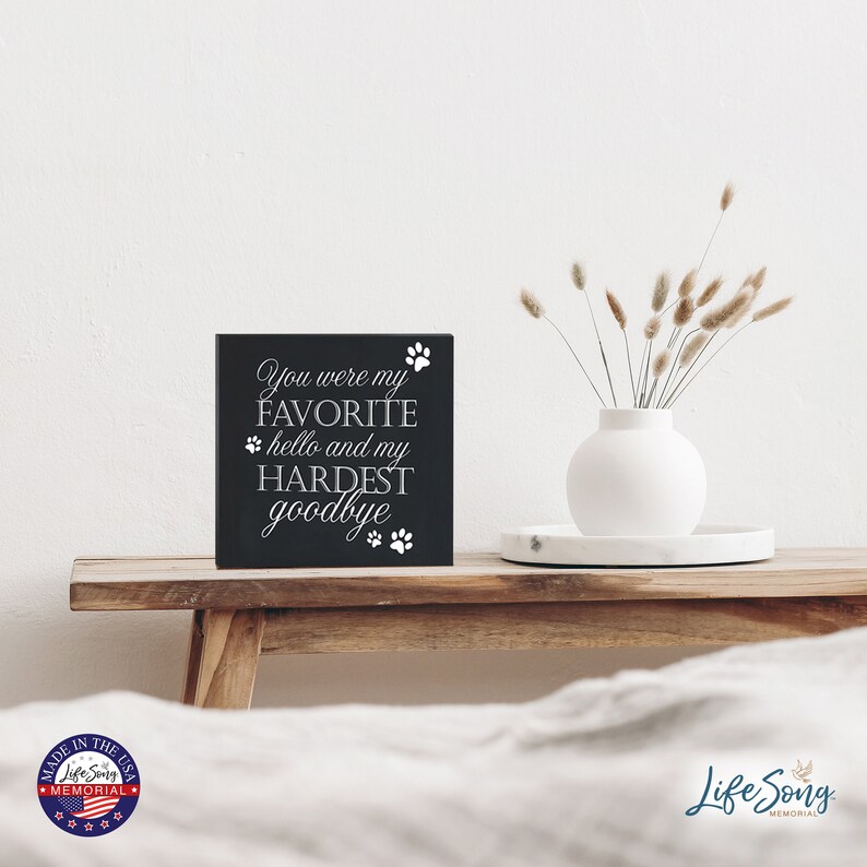 May include: Black wooden sign with white text that reads "You were my FAVORITE hello and my HARDEST goodbye" with paw prints around the text.