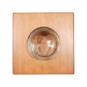 May include: A square wooden tray with a round glass inset. The tray is a light brown color and the glass is clear.
