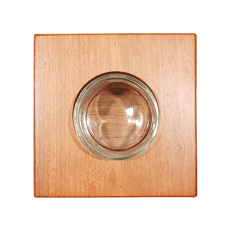 May include: A square wooden tray with a round glass inset. The tray is a light brown color and the glass is clear.