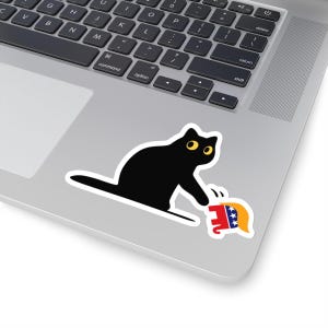 May include: A black cat with yellow eyes is swatting at a red, white, and blue elephant figurine. The cat and elephant are on a silver laptop.