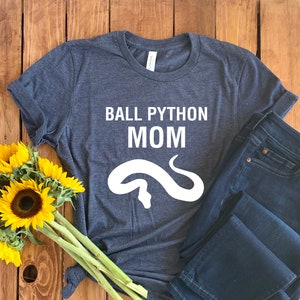 Peut inclure: Un t-shirt bleu foncé avec le texte "BALL PYTHON MOM" et un contour blanc d'un serpent sur le devant.