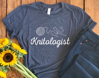 May include: A dark blue t-shirt with a white graphic of a ball of yarn and knitting needles. The text "Knit-ologist" is printed below the graphic.