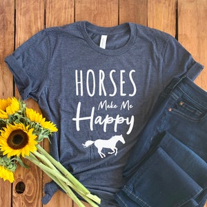 May include: A dark blue t-shirt with the text "Horses Make Me Happy" in white lettering and a white silhouette of a horse running. The shirt is laid out on a wooden surface with a bouquet of sunflowers.