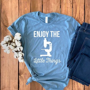 May include: A light blue t-shirt with a white graphic of a microscope and the text "Enjoy the Little Things".