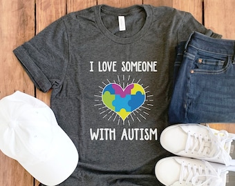 May include: A dark grey t-shirt with the text "I love someone with autism" and a colorful puzzle piece heart graphic.