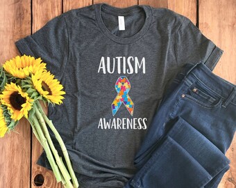 May include: A dark grey t-shirt with the text "AUTISM AWARENESS" and a blue, green, yellow, and red puzzle piece ribbon.