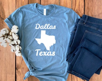 May include: A light blue t-shirt with a white outline of the state of Texas and the text "Dallas Texas" in white.