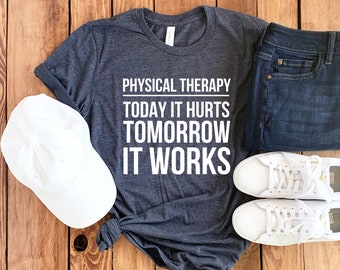 May include: A dark gray t-shirt with the text "PHYSICAL THERAPY TODAY IT HURTS TOMORROW IT WORKS" in white. The shirt is paired with white sneakers, blue jeans, and a white baseball cap.