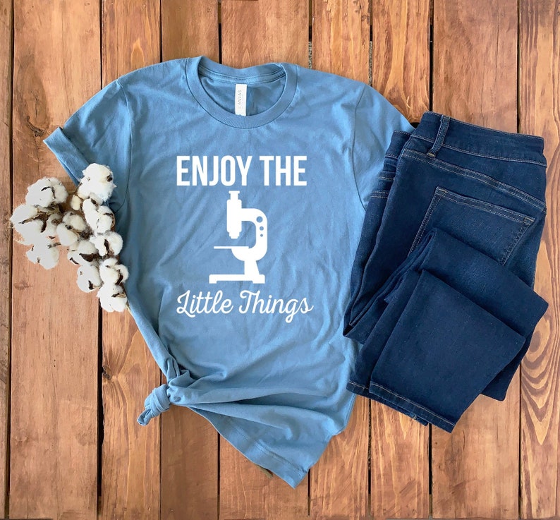 May include: A light blue t-shirt with a white graphic of a microscope and the text "Enjoy the Little Things".