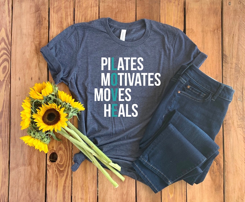 May include: A dark blue t-shirt with white text that reads "PILATES MOTIVATES MOVES HEALS" with the word "LOVE" in teal.