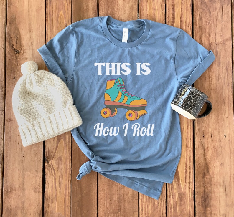 K&ouml;nnte beinhalten: Ein blaues T-Shirt mit dem Text "This is How I Roll" und einer Grafik eines Rollschuhs. Der Rollschuh ist gelb, orange, gr&uuml;n und blau.
