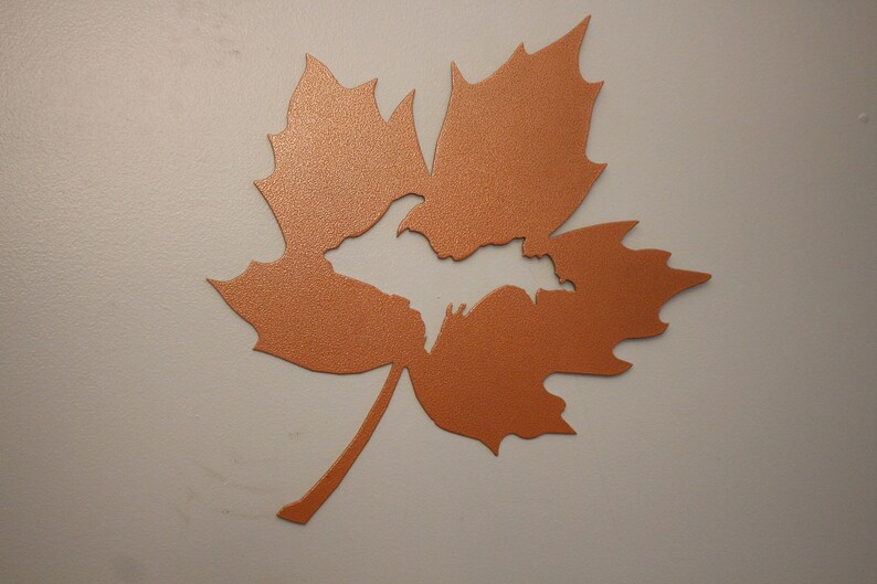 May include: A copper-colored metal maple leaf with a cut-out shape of the Upper Peninsula of Michigan.