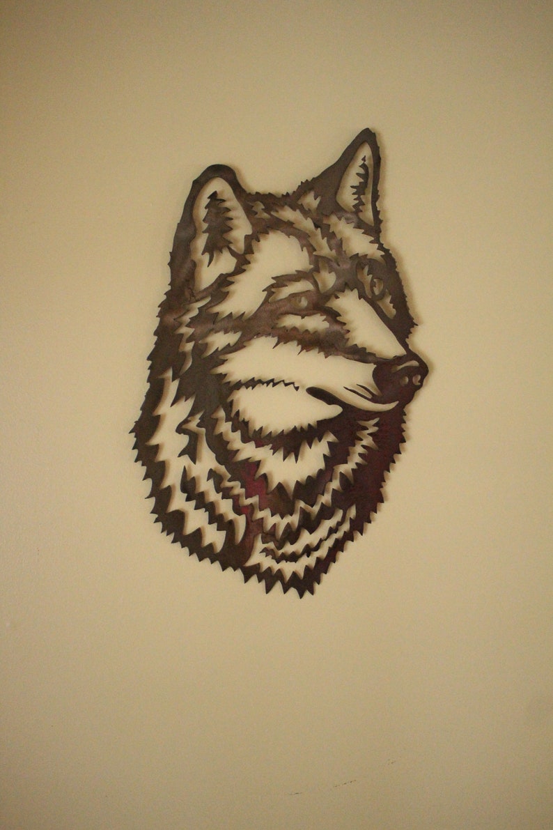 Op de afbeelding: Een metalen wandsculptuur van een wolfskop, met een gedetailleerd, gestructureerd ontwerp. De wolfskop is naar rechts gericht, met een gesloten bek en gesloten ogen.