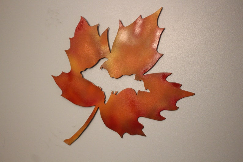 May include: A metal maple leaf wall decor with a cutout of the Upper Peninsula of Michigan in the center. The leaf is painted in shades of orange and red.