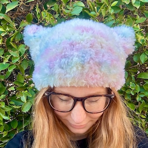 May include: A fluffy pastel tie-dye beanie with fuzzy ear flaps. The beanie is made of soft, plush fabric and has a light blue, pink, and yellow color scheme.