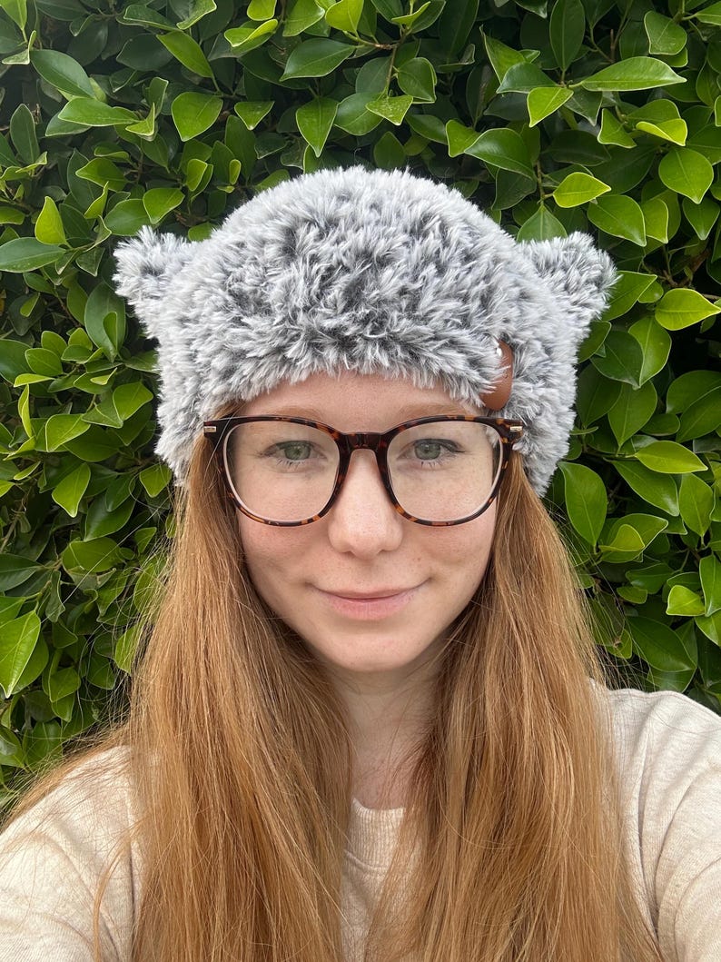 May include: A gray and white fuzzy knit hat with ear flaps and a brown button on the side.