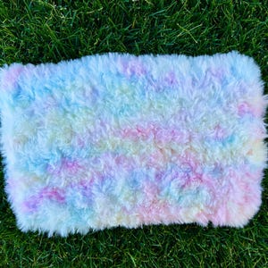 May include: A fluffy, pastel-colored rug with a tie-dye pattern. The rug is made of soft, white fur and has shades of pink, blue, and yellow.