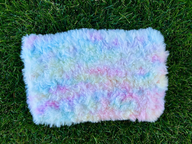 May include: A fluffy, pastel-colored rug with a tie-dye pattern. The rug is made of soft, white fur and has shades of pink, blue, and yellow.
