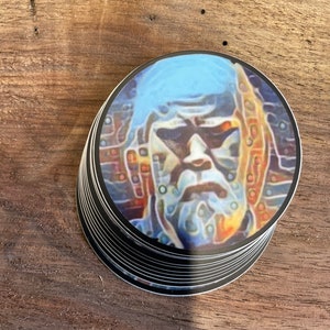 May include: A stack of round stickers with a colorful, abstract portrait of a person with a blue background.