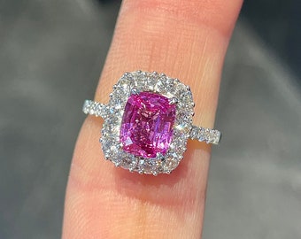 May include: A ring featuring a rectangular cushion-cut vibrant pink center stone surrounded by a halo of small round white stones. The band is made of a silver-toned metal and is also set with small round white stones along the visible shank.