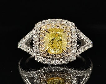 May include: A luxurious ring featuring a large, cushion-cut yellow diamond center stone, surrounded by a double halo of smaller white diamonds. The split shank band is also adorned with diamonds, creating a dazzling display of light.