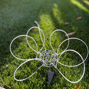 May include: A white fishing net with six loops and a lead weight attached to the bottom. The net is lying on green grass.