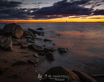 Reflections of a fiery sunrise over the Chesapeake Bay at Sandy Point State Park in Maryland by the Bay Bridge. Visible is Sandy Point Light