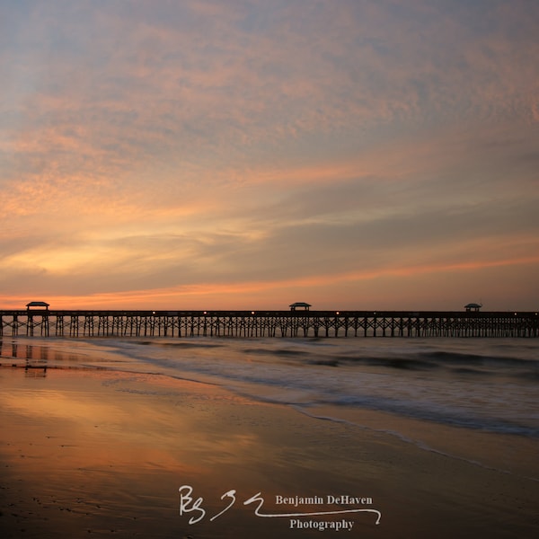 An electric morning sunrise at the Folly Beach Fishing Pier in South Carolina. A sandy beach on the Atlantic Ocean.