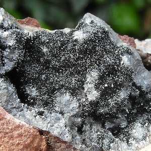 Puede incluir: Primer plano de una roca negra con cristales plateados. Los cristales están agrupados y tienen un aspecto brillante.