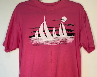 May include: Pink t-shirt featuring a white graphic of sailboats on the water with a moon in the sky. The graphic says "Hawaii" underneath the sailboats.