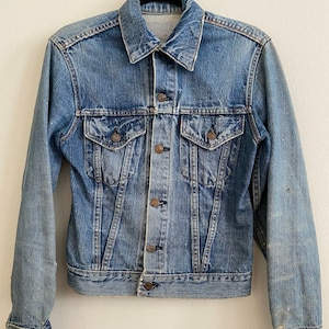 Puede incluir: Una chaqueta vaquera vintage con un diseño clásico. La chaqueta es azul y tiene un aspecto descolorido. Tiene cierre de botones y dos bolsillos delanteros.