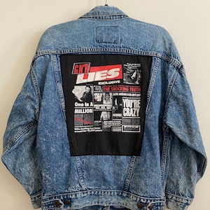 May include: A blue denim jacket with a black and red patch on the back. The patch features a newspaper-style design with the text "GN'R LIES EXCLUSIVE THE SHOCKING TRUTH" and other text.