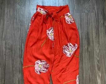 Puede incluir: Pantalón rojo de cintura alta con estampado floral de tulipes rosas. El pantalón tiene un lazo en la cintura.