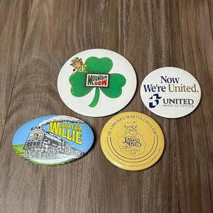 May include: Four different button pins. One is a green shamrock with the words "Mountain Dew" inside. Another is a yellow circle with the words "I'm a Precious Moments Collector" and a picture of a Precious Moments figurine. The third is a blue oval with a picture of a train and the words "Box Car Willie". The last is a white circle with the words "Now We're United" and the number "3" with the words "United Medical Center" underneath.