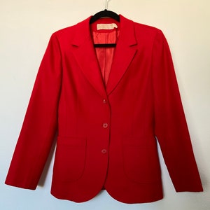 May include: A red blazer with a single button closure and two flap pockets. The blazer is hanging on a black hanger.