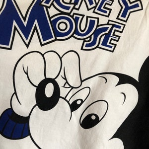 May include: White t-shirt with a black and blue Mickey Mouse graphic. The text "Mickey Mouse" is printed in blue with a black outline.