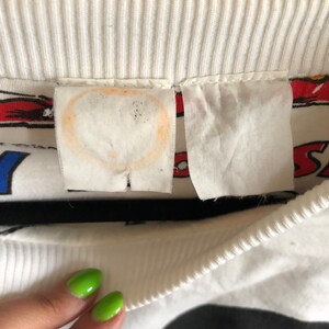 May include: White sweatshirt with a black and white Mickey Mouse graphic print. The sweatshirt has a ribbed crew neck and a white tag with a stain.