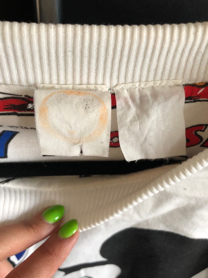 May include: White sweatshirt with a black and white Mickey Mouse graphic print. The sweatshirt has a ribbed crew neck and a white tag with a stain.