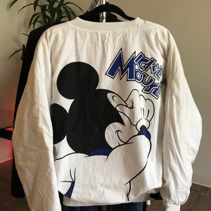 May include: White long-sleeve sweatshirt with a black and white Mickey Mouse graphic and the text "Mickey Mouse" in blue lettering.
