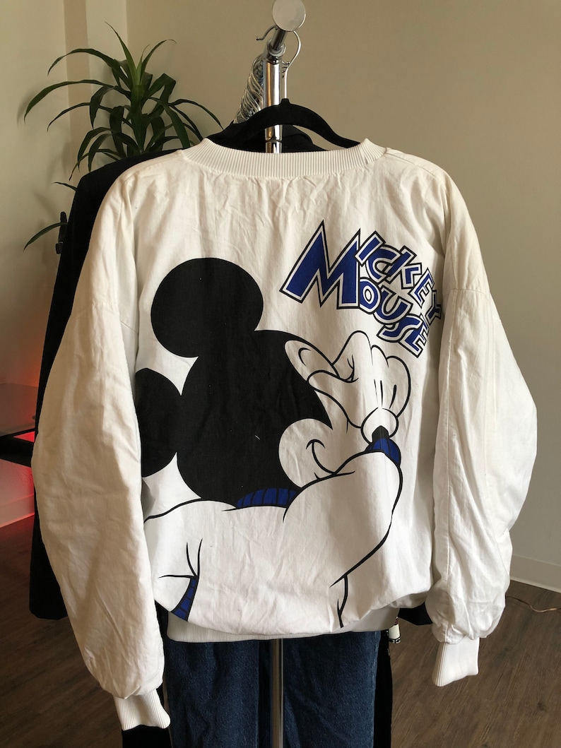 May include: White long-sleeve sweatshirt with a black and white Mickey Mouse graphic and the text "Mickey Mouse" in blue lettering.