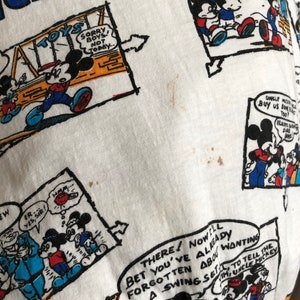 May include: White t-shirt with a repeating pattern of Mickey Mouse cartoon illustrations. The illustrations feature Mickey Mouse in various poses and settings, including playing with toys, riding a swing set, and interacting with other characters. The text "Mickey Mouse" is printed in blue at the top of the shirt.