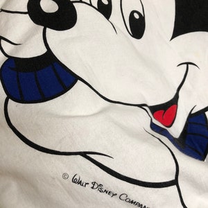 May include: White t-shirt with a cartoon image of Mickey Mouse wearing a blue and white striped scarf. The text "Walt Disney Company" is printed in black at the bottom of the shirt.